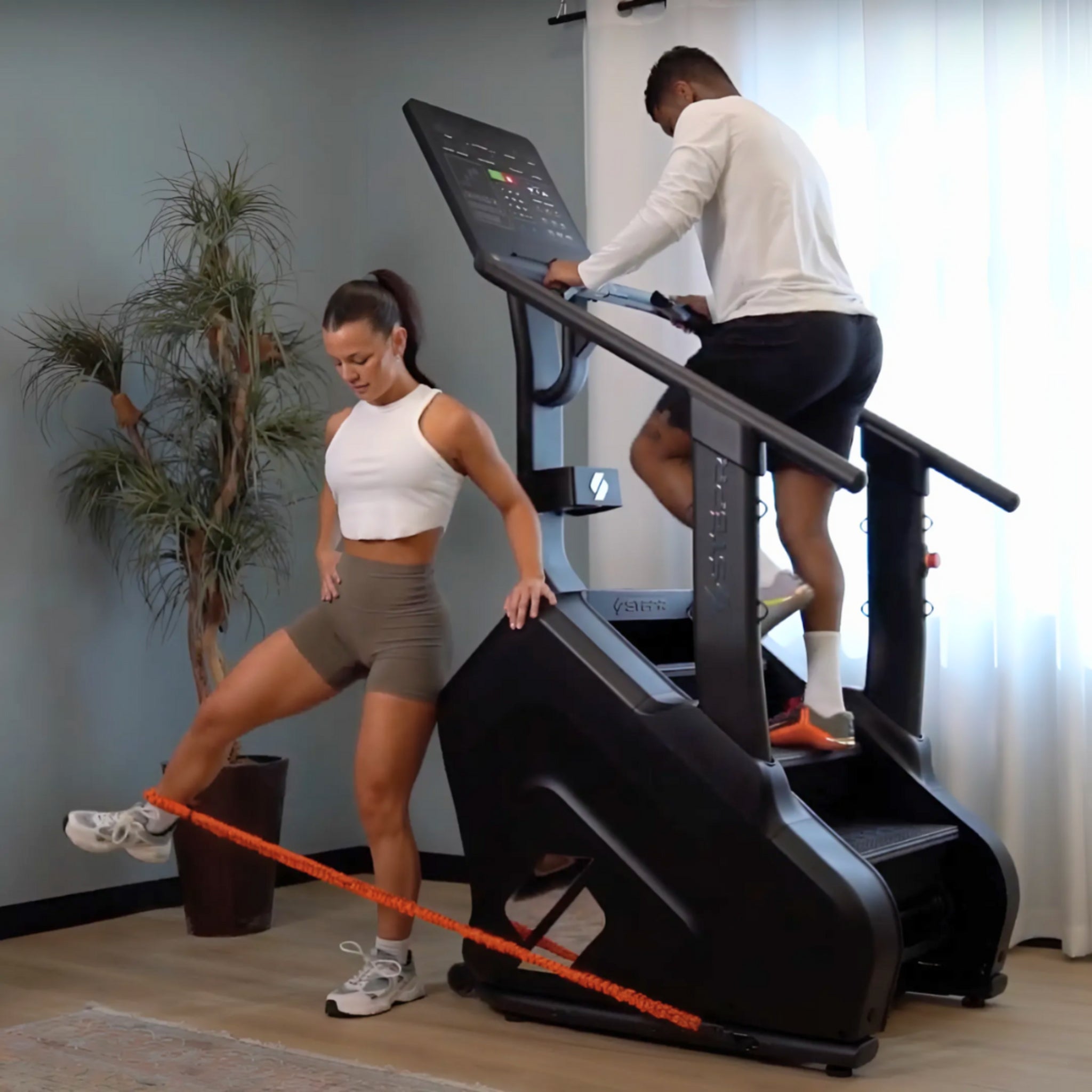 Man and woman exercising on the STEPR Pro stair climber with HD touchscreen in a modern home gym setting for cardio and strength training.