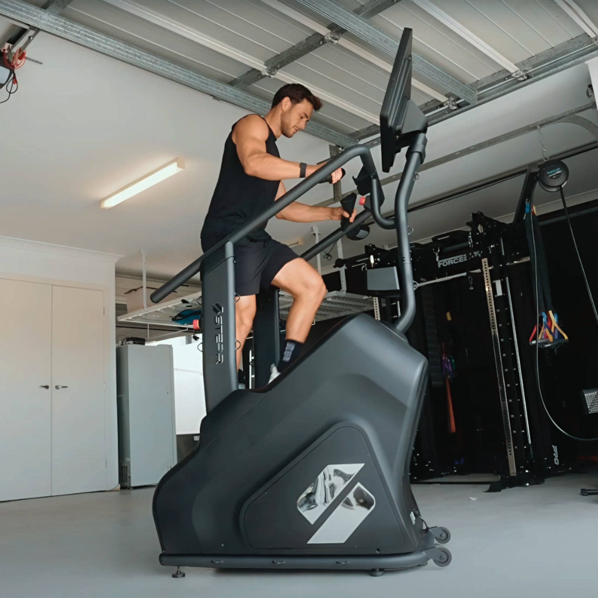 Man training on the STEPR Pro + stair climber with HD touchscreen in a garage gym setup for cardio and endurance fitness.
