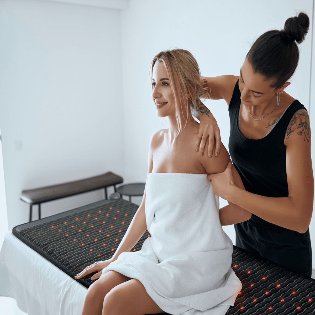 Woman receiving a back massage while sitting on a PEMF infrared heating mat with red light therapy in a spa setting