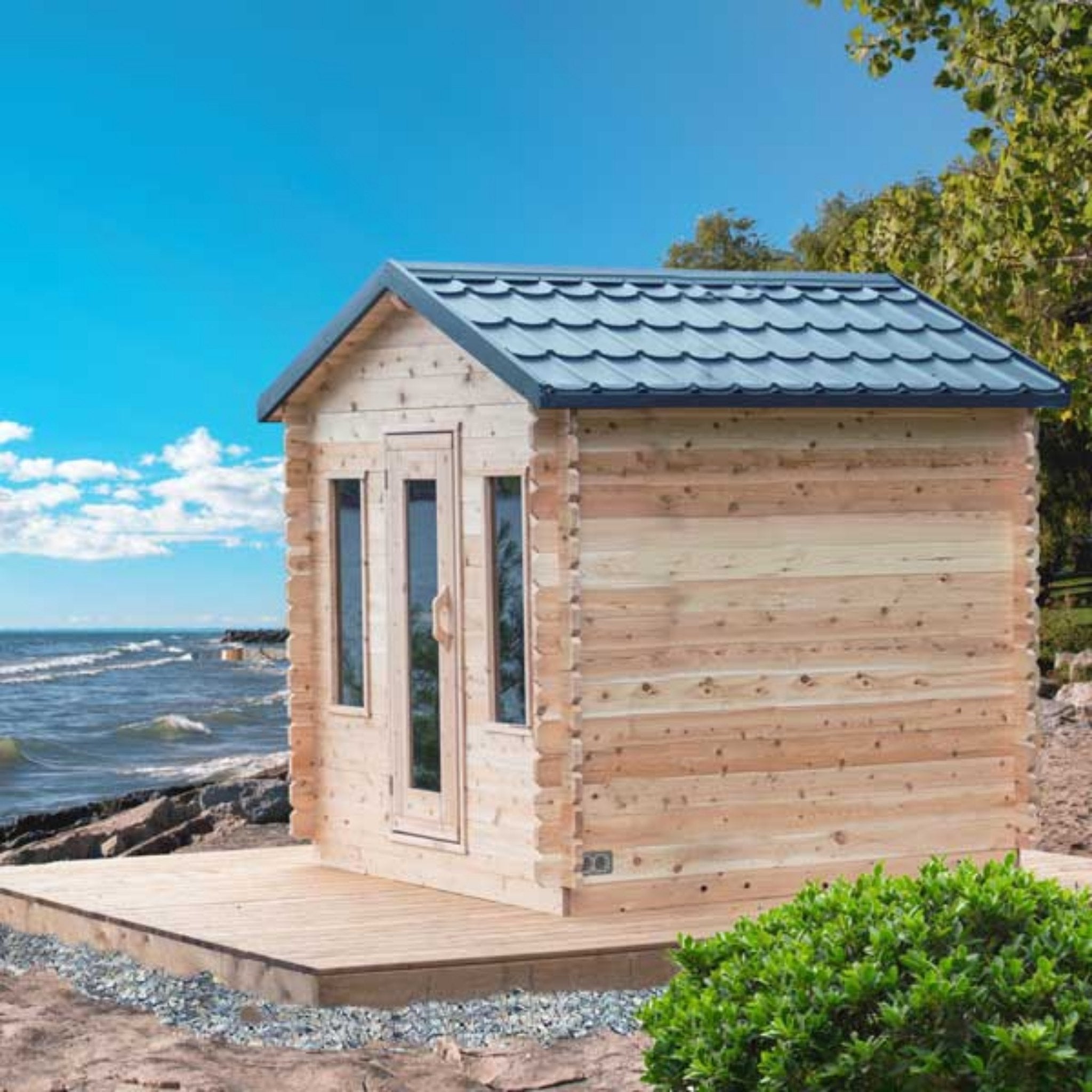 Leisurecraft CT Georgian Cabin Sauna with front windows and cedar deck, positioned by the water with clear blue sky and natural surroundings.