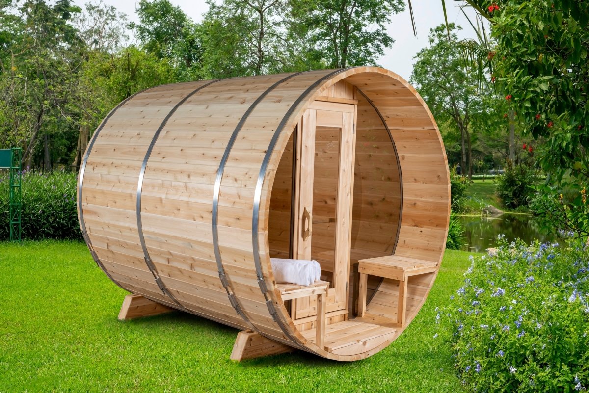 Leisurecraft Serenity MP Barrel Sauna with rounded cedar staves, front glass door, and small porch seating, set on lush green grass in a natural garden environment.