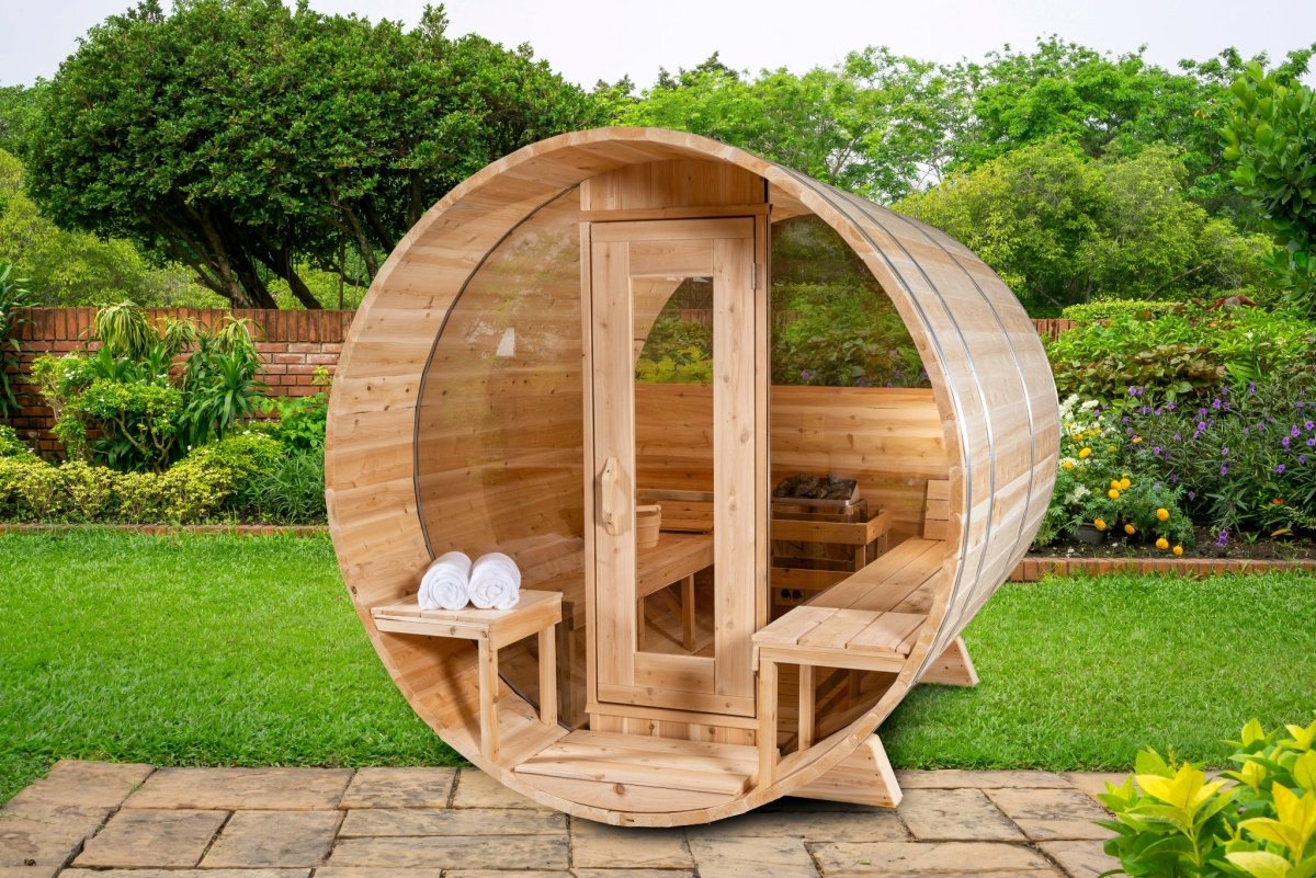 Leisurecraft Serenity MP Barrel Sauna with open glass door revealing cedar benches, set on a paved patio surrounded by lush green garden scenery.