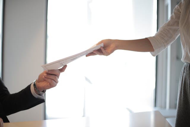 Person handing over a document to another person in an office setting
