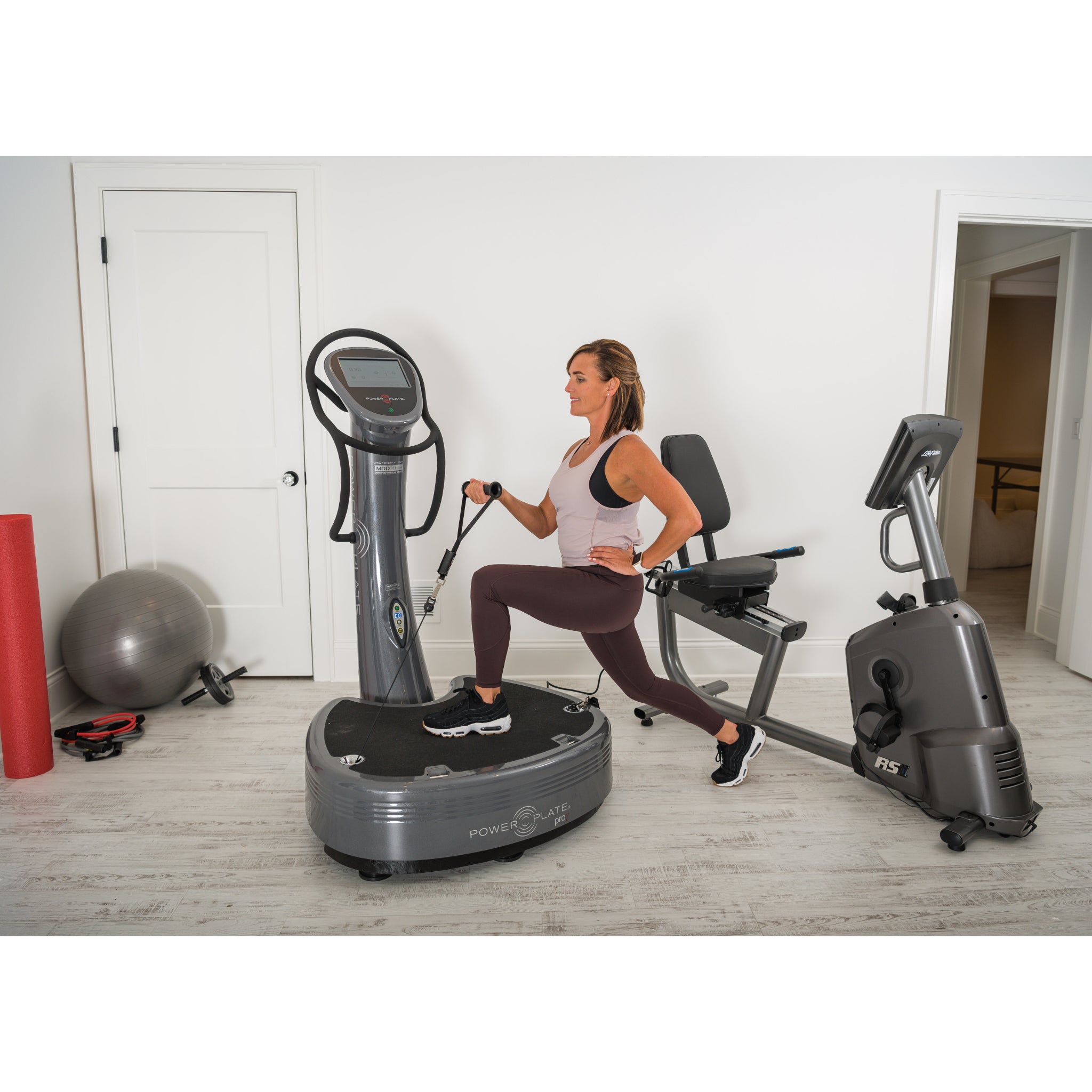 Woman performing a lunge exercise on the Power Plate pro7 vibration training machine in a home gym setting