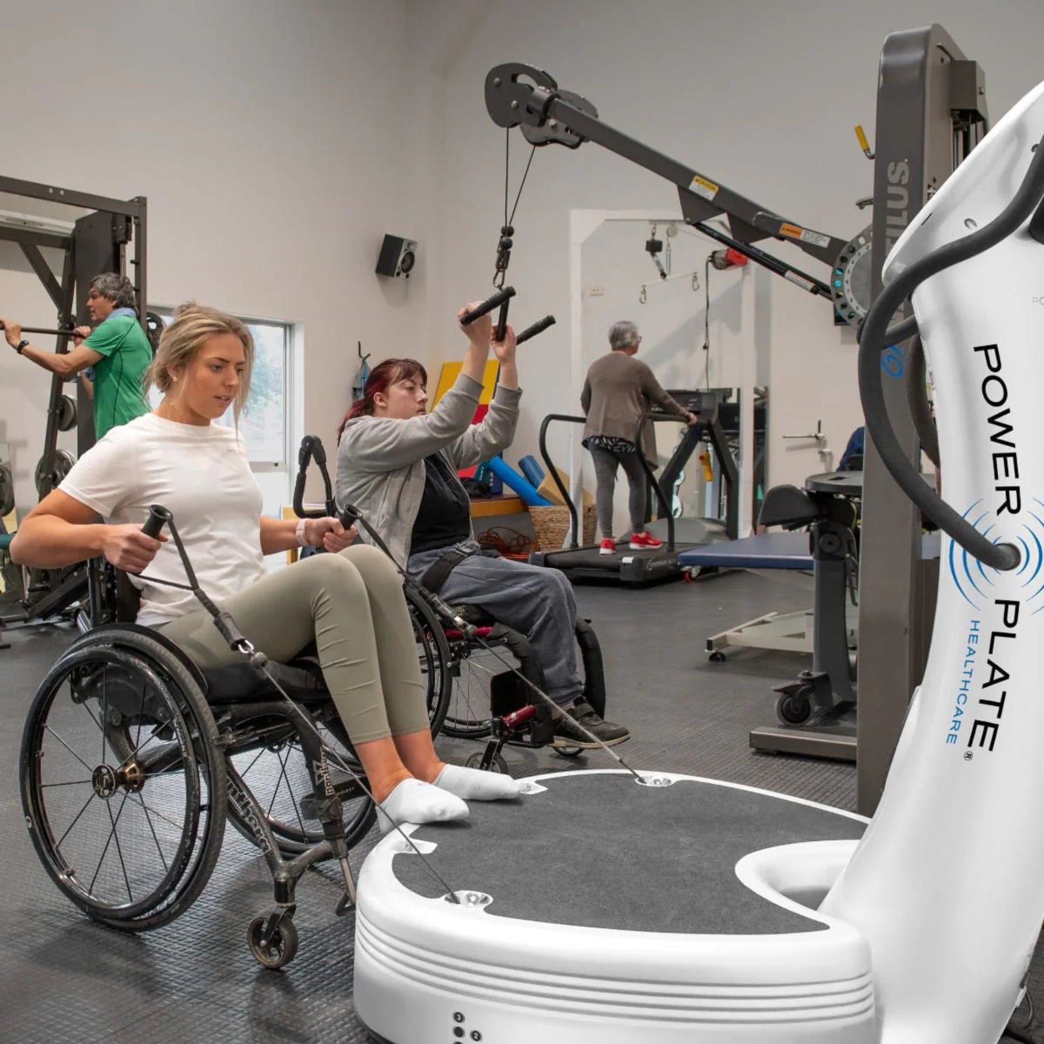 Woman in a wheelchair exercising with the Power Plate pro7HC white vibration training machine in a gym setting