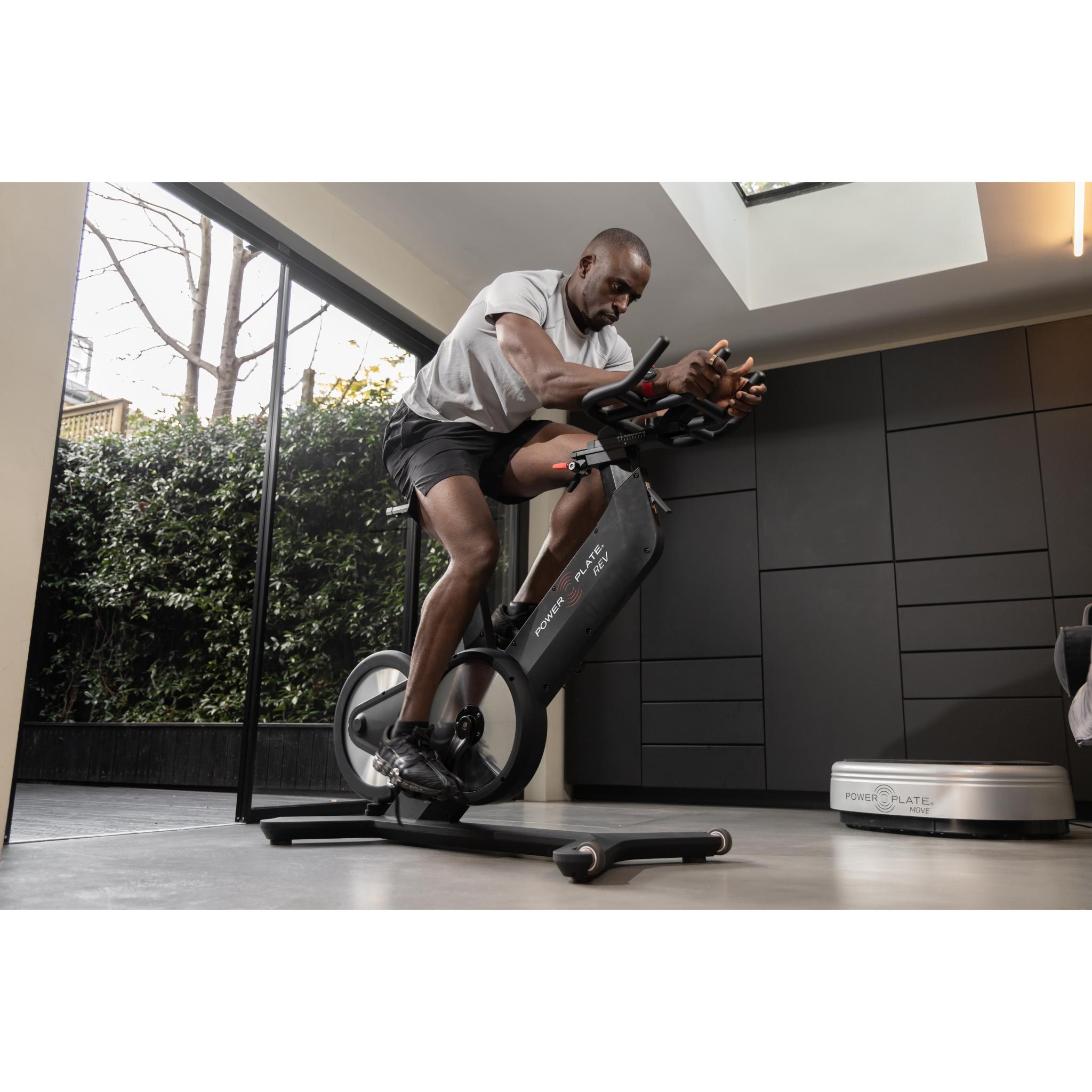 Man exercising on the Power Plate REV black vibration training bike in a modern home gym with natural light