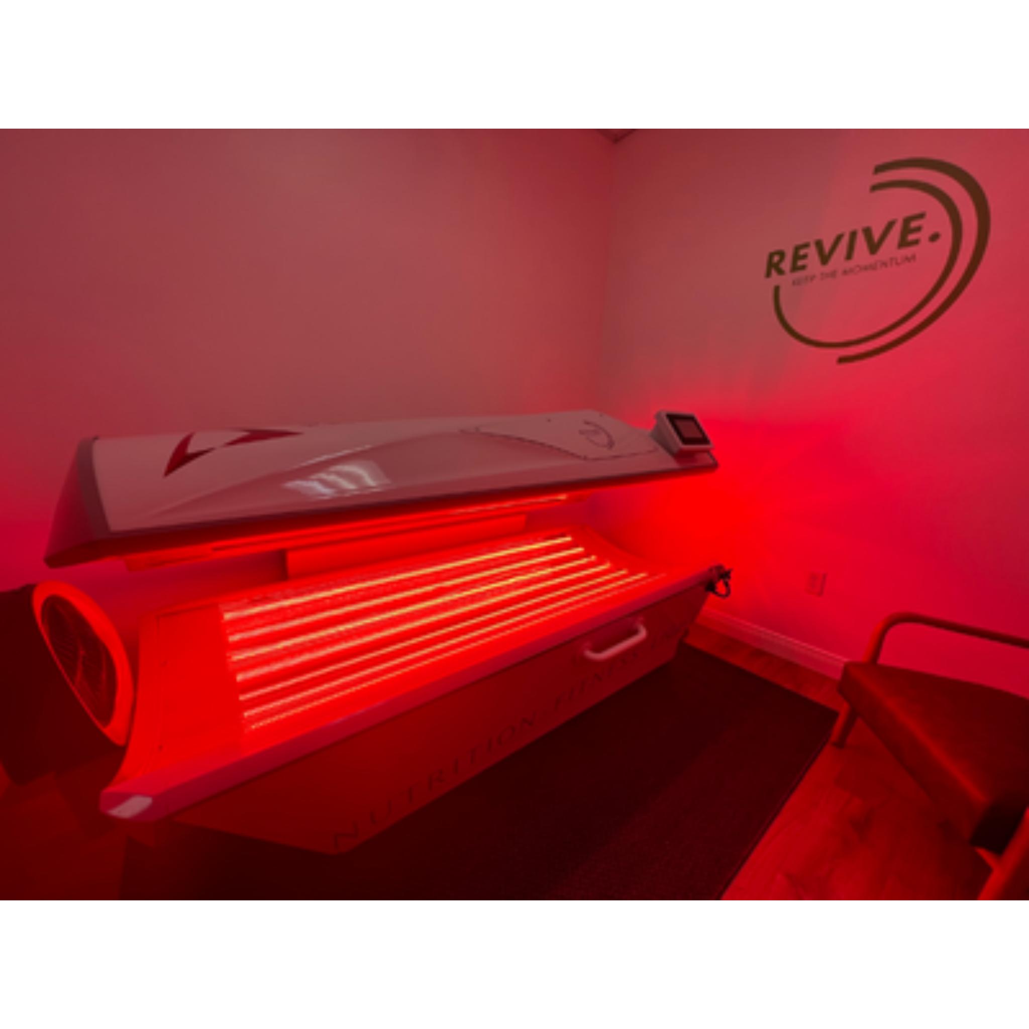 Prism Light Pod closed with glowing red light panels and REVIVE branding in a wellness treatment room