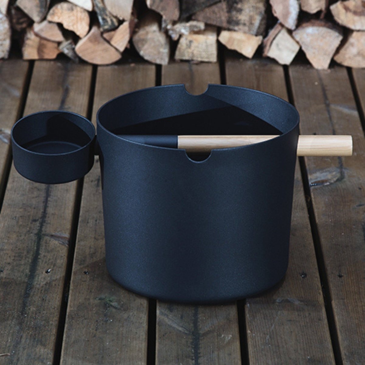 SaunaLife Accessory Package 6 black sauna bucket and ladle displayed outdoors beside a woodpile.