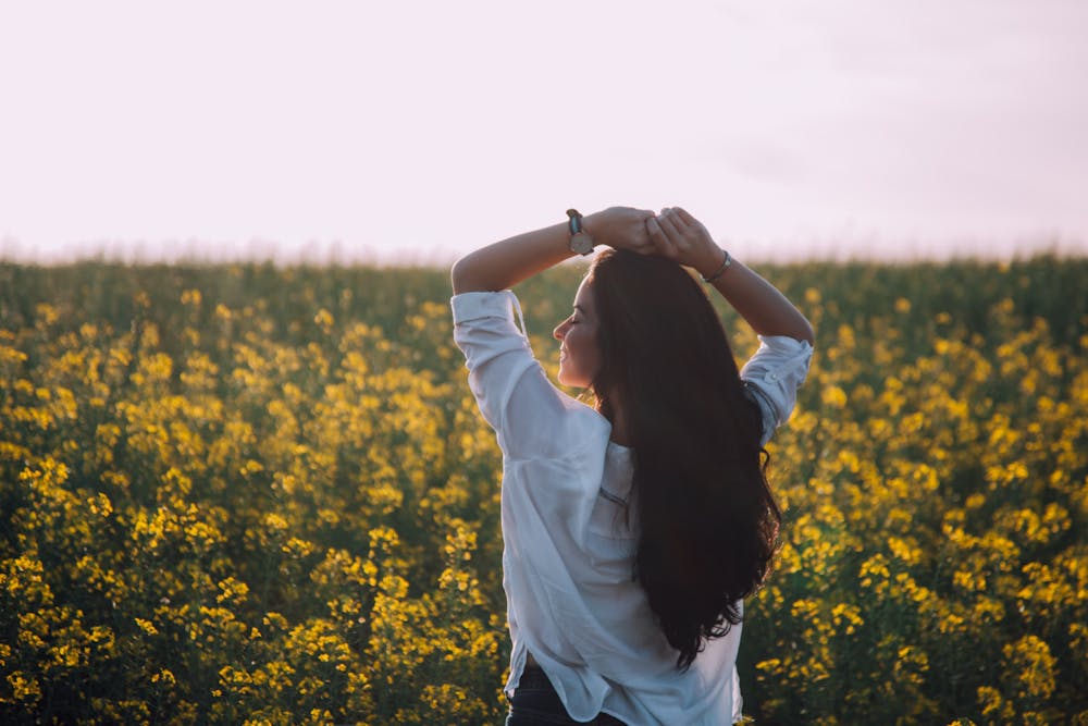 Woman standing in a field of yellow flowers with her arms raised, enjoying the moment.