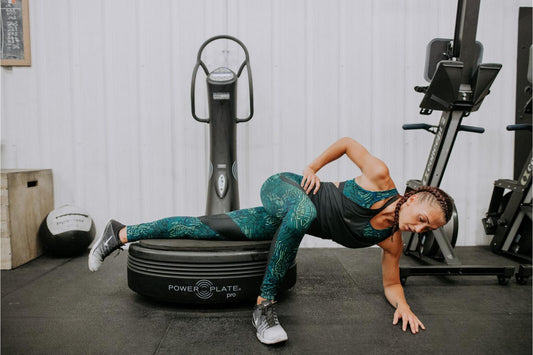 Woman performing a side plank on a Power Plate vibration platform in a home fitness space