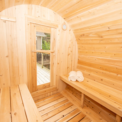 Interior of a cedar barrel sauna featuring wooden benches, a side window with outdoor deck view, and neatly rolled towels.