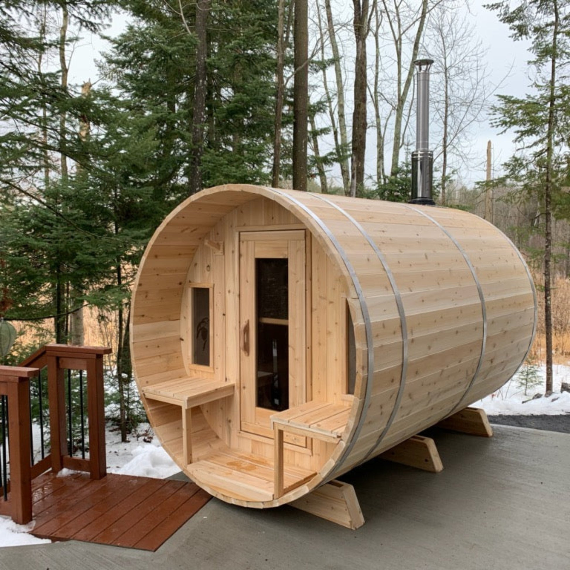 Leisurecraft Canadian Timber barrel sauna in natural wood finish, displayed outdoors on a deck with glass door and benches inside, highlighting premium craftsmanship