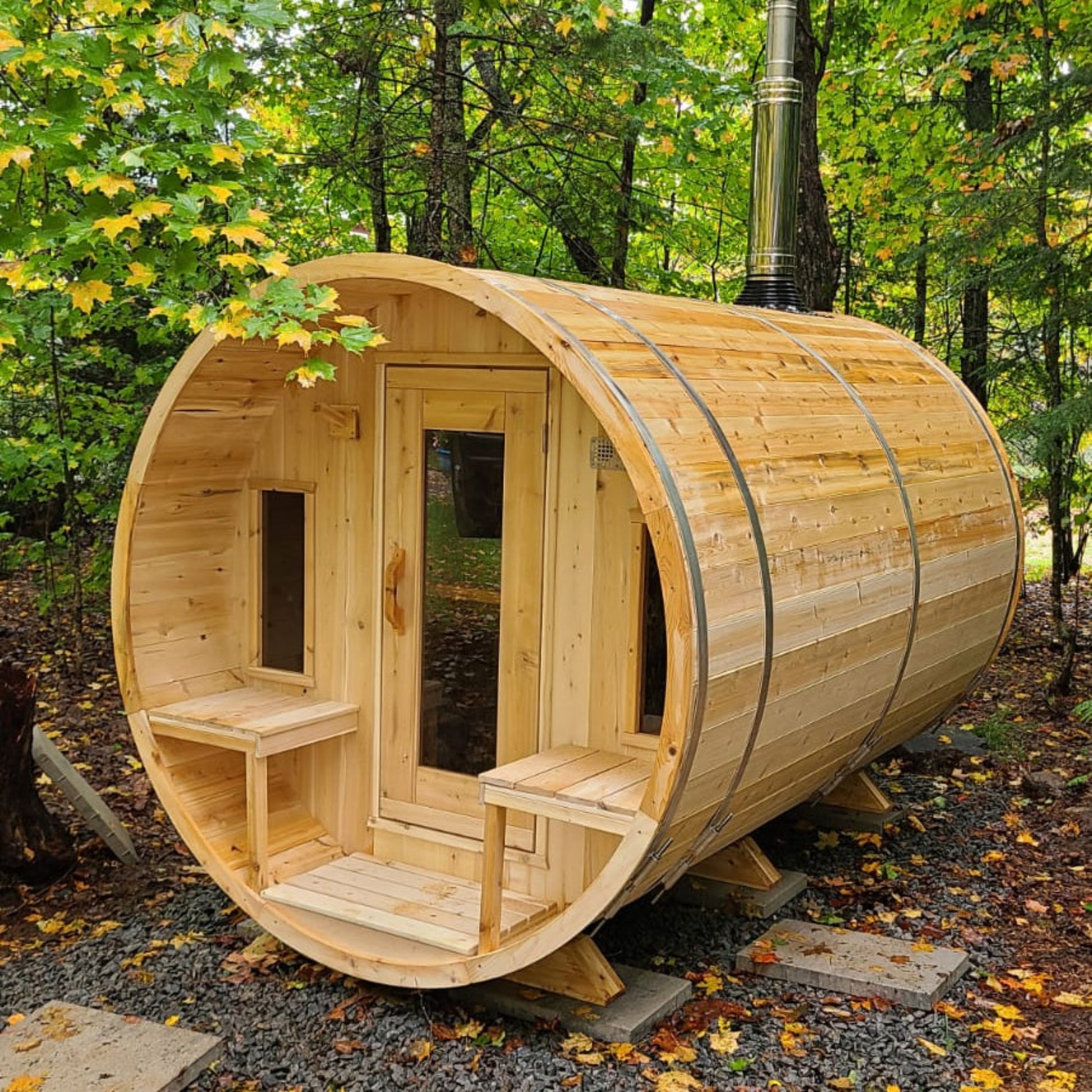 Leisurecraft Canadian Timber barrel sauna in natural wood finish, showcased outdoors in a forest setting with glass door and benches inside, highlighting authentic craftsmanship