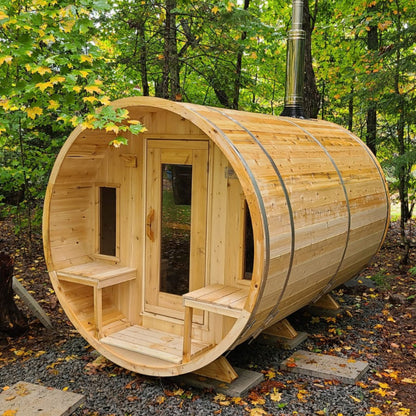 Leisurecraft Canadian Timber barrel sauna in natural wood finish, showcased outdoors in a forest setting with glass door and benches inside, highlighting authentic craftsmanship