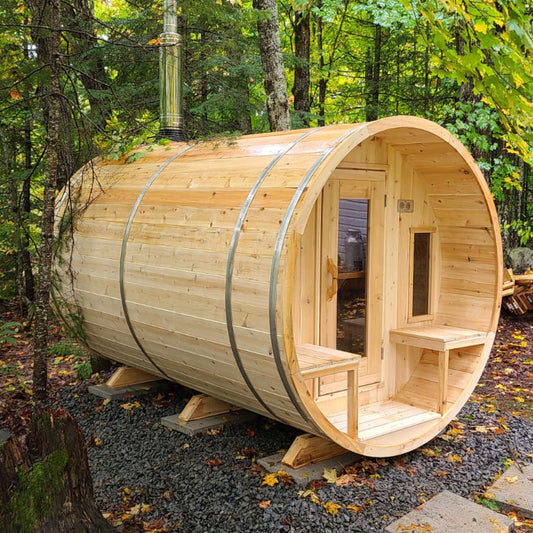 Leisurecraft Canadian Timber barrel sauna made of natural wood, showcased outdoors in a forest setting with open door and benches inside, highlighting authentic craftsmanship