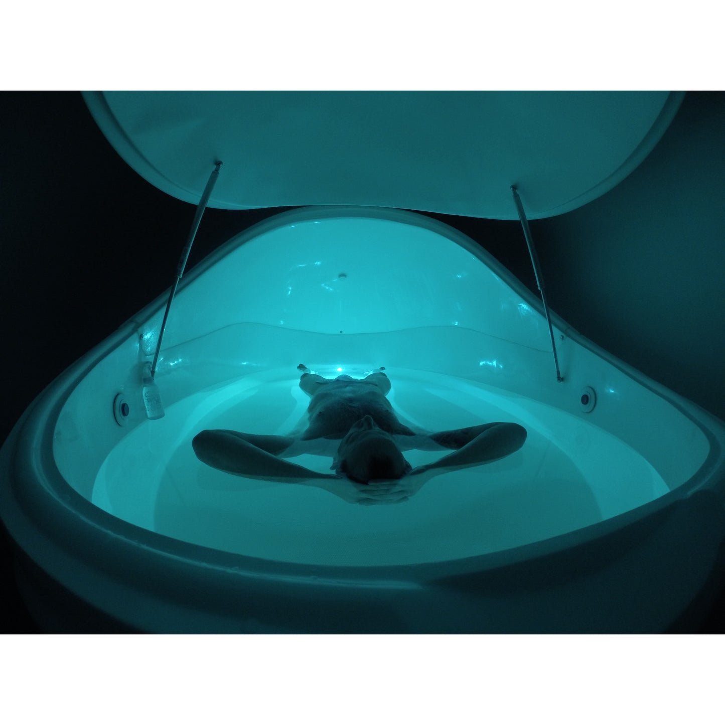Person floating inside Dreampod float pod with open canopy lid, illuminated with calming blue LED lighting, creating a deep relaxation and sensory therapy experience