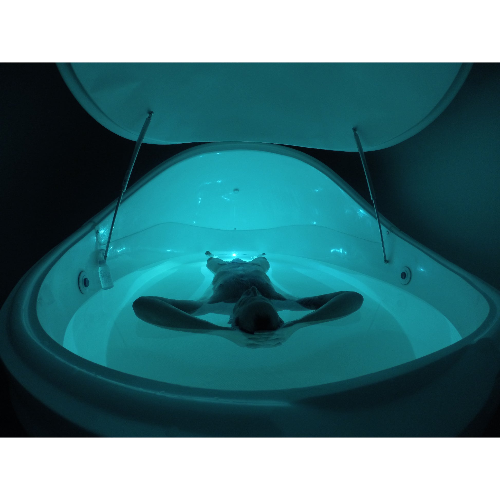Person floating inside Dreampod float pod with open canopy lid, illuminated with calming blue LED lighting, creating a deep relaxation and sensory therapy experience
