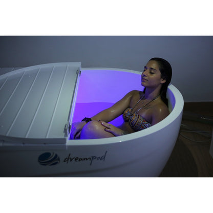 Woman relaxing in a Dreampod ice bath with purple LED lighting, partially closed lid, and Dreampod branding visible