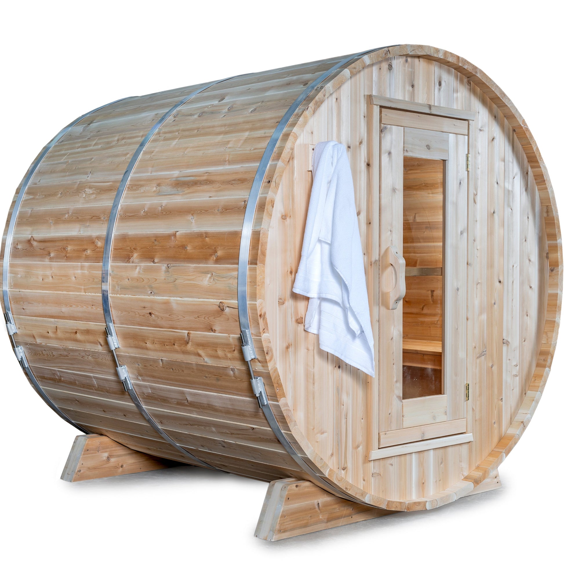 Outdoor cedar barrel sauna with a front glass door and towel hanging on the handle, shown on a white background.