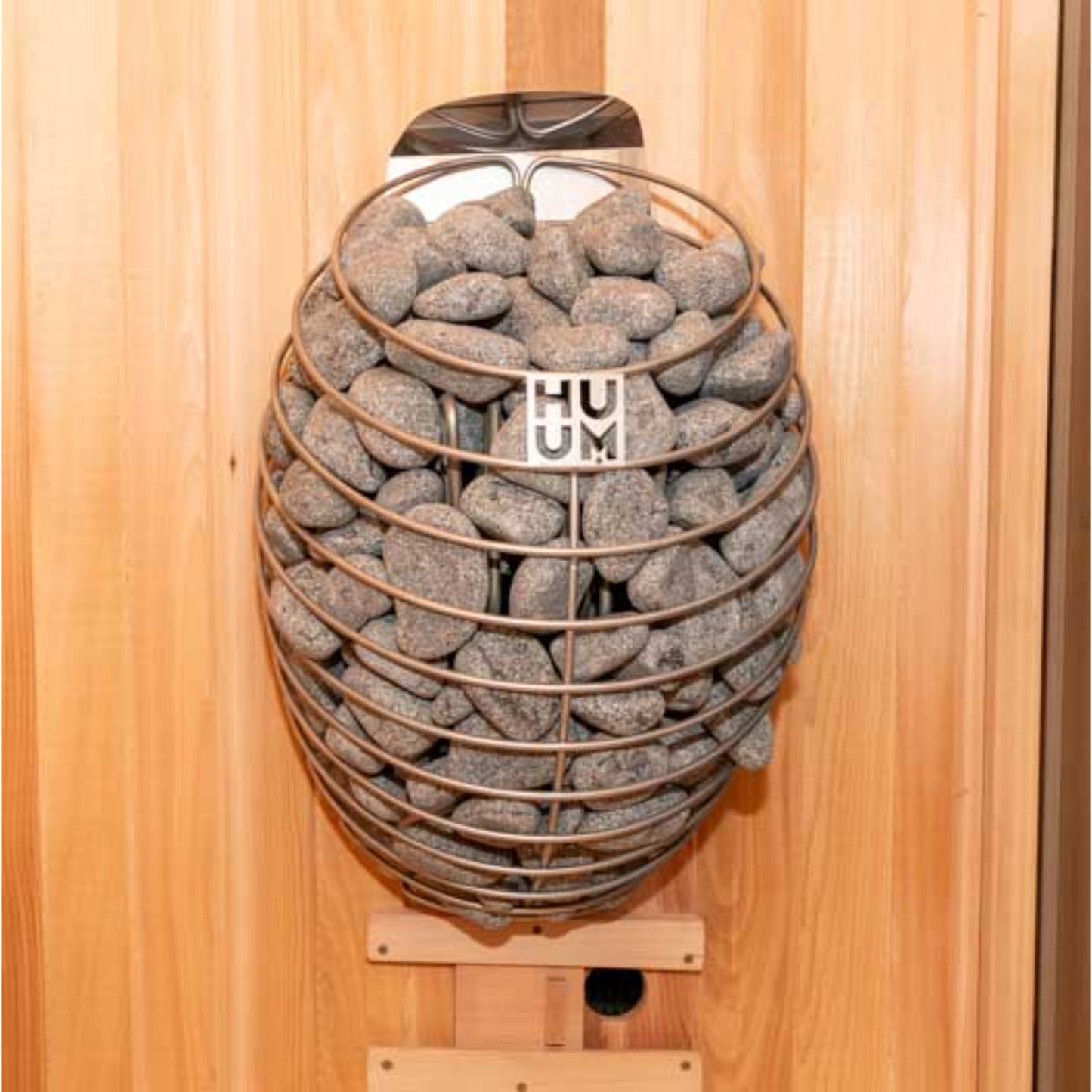 Modern HUUM DROP 9kW wall-mounted sauna heater filled with natural stones against a wooden panel background