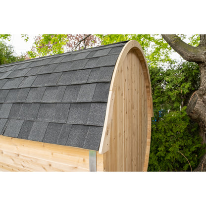 Close-up of a Leisurecraft barrel sauna with a gray shingle roof, set outdoors beside trees