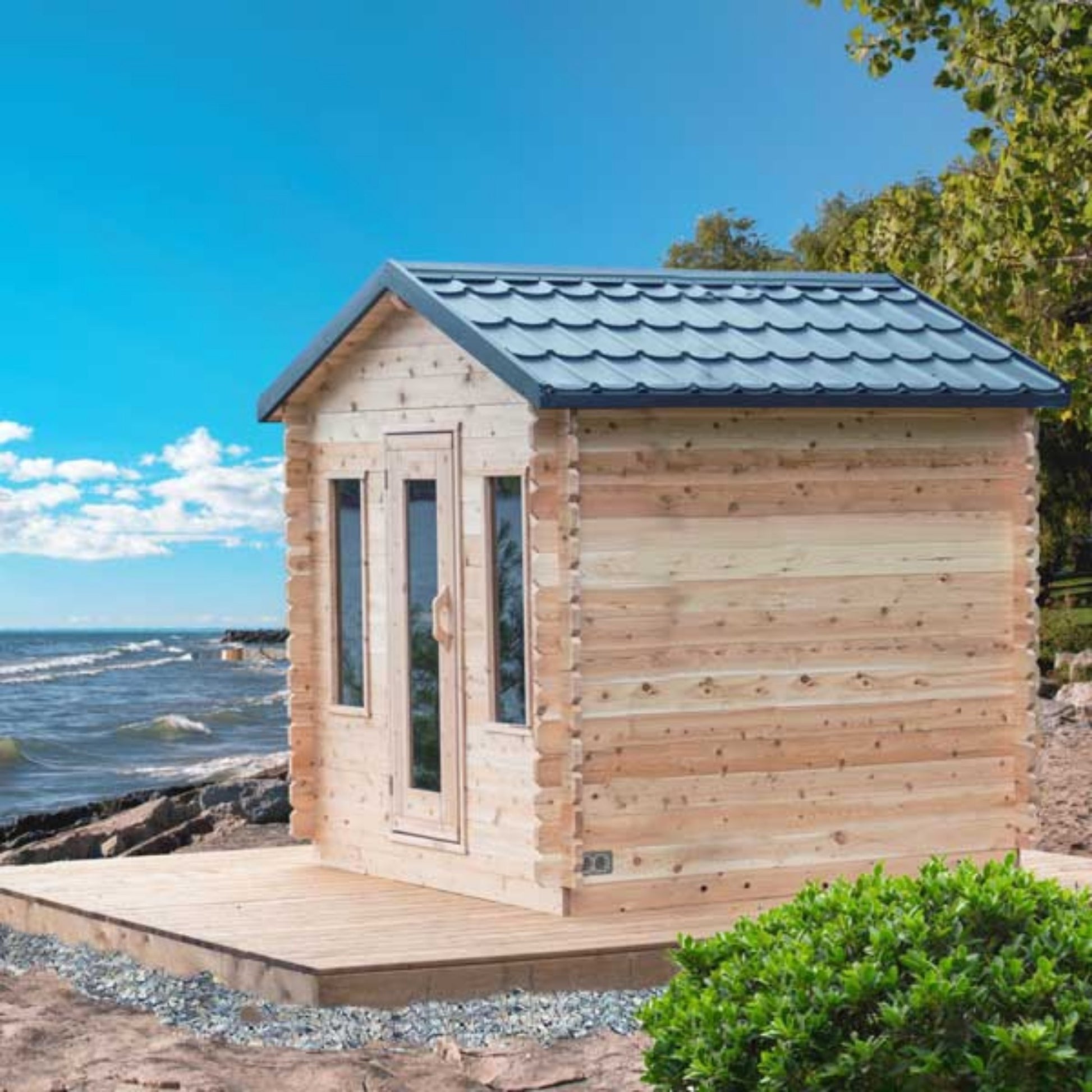 Leisurecraft CT Georgian Cabin Sauna with front windows and cedar deck, positioned by the water with scenic sky and natural surroundings