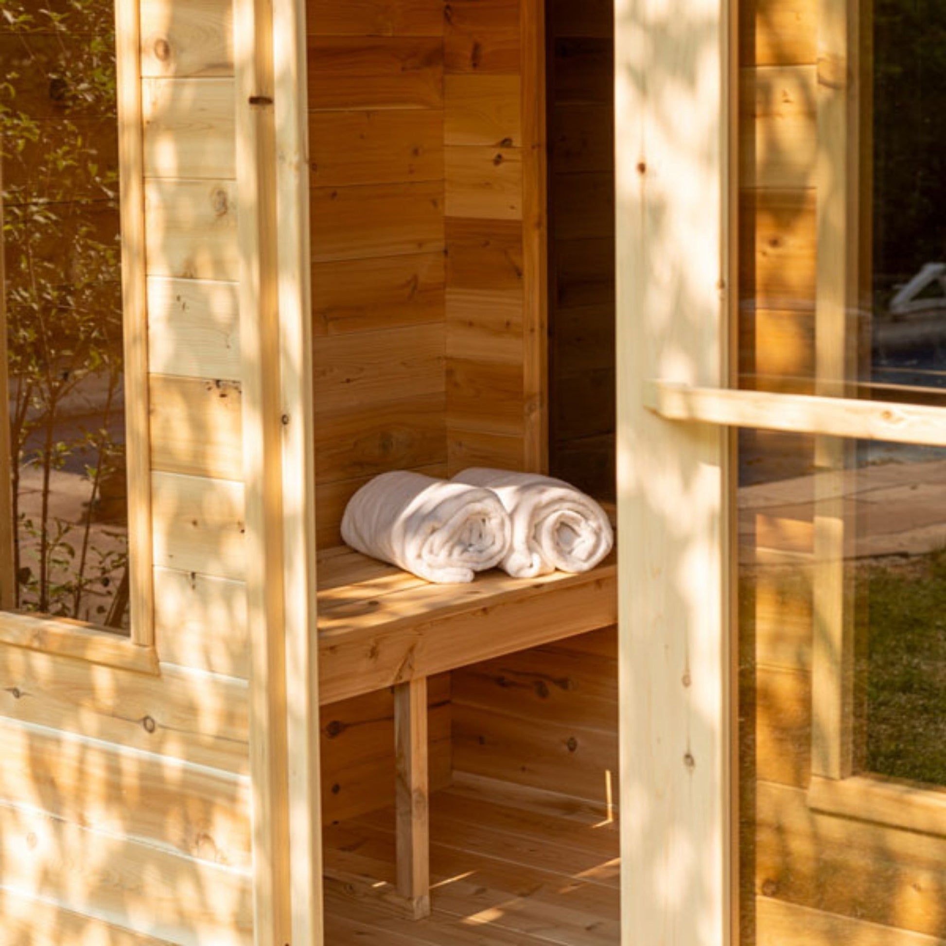 Interior of the Leisurecraft CT Georgian Cabin Sauna changeroom with cedar bench, rolled white towels, and view into the main sauna area