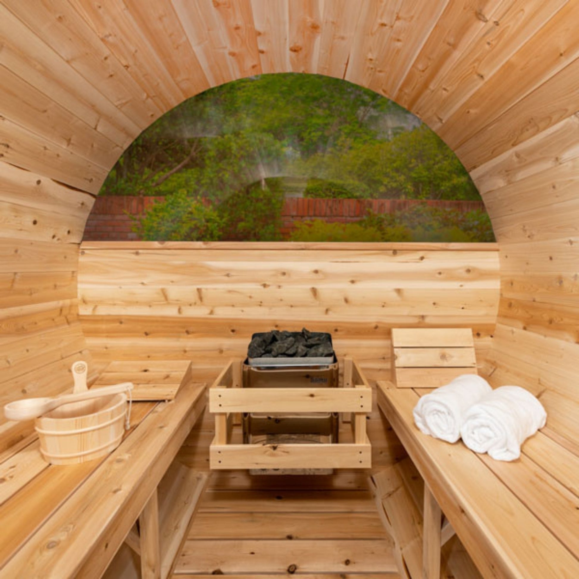 Wooden barrel sauna interior with cedar benches, sauna heater, and towels placed on both sides