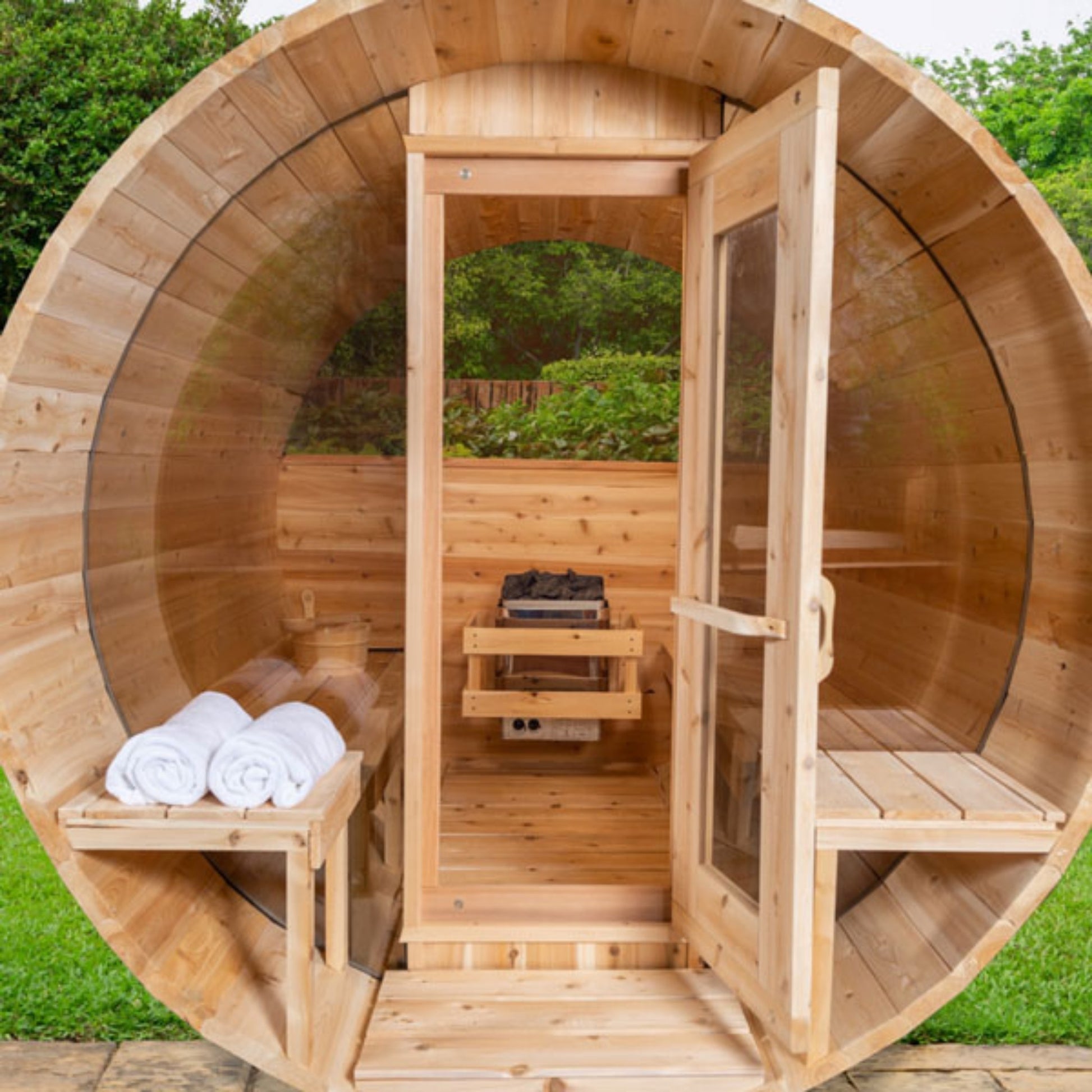 Outdoor wooden barrel sauna with open glass door, interior benches, and towels placed near the entrance