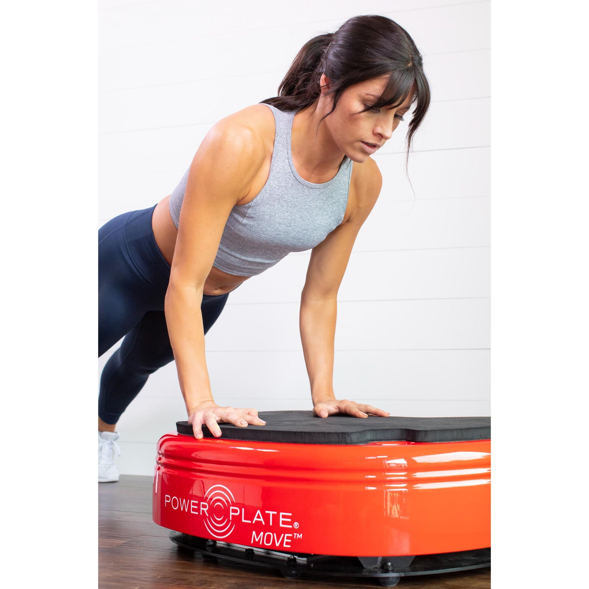 Woman performing a push-up on a red Power Plate MOVE vibration plate in a home workout setting