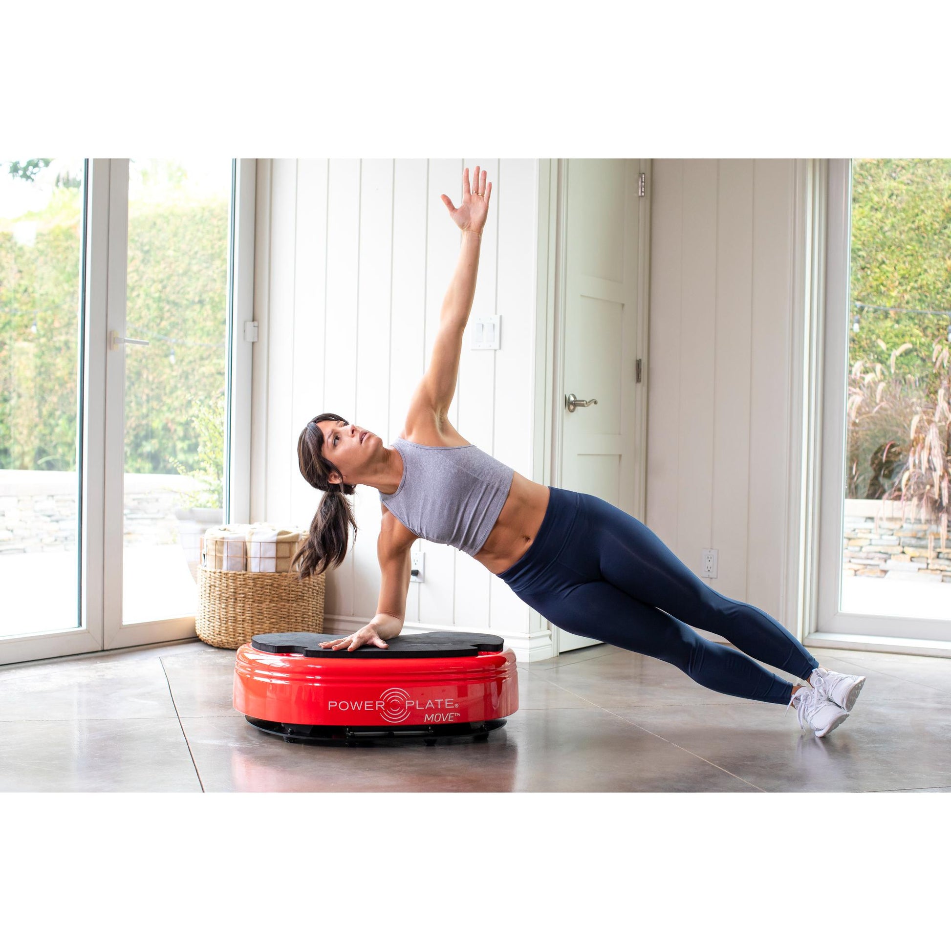 Woman performing a side plank on a red Power Plate MOVE vibration plate in a bright home workout space
