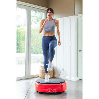 Woman performing a step exercise on a red Power Plate MOVE vibration plate in a bright home workout space