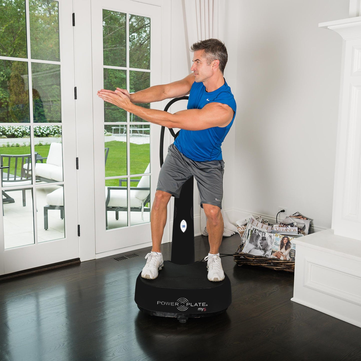 Man exercising on a black Power Plate my5 vibration plate with straight handlebars in a bright home setting, near large glass doors