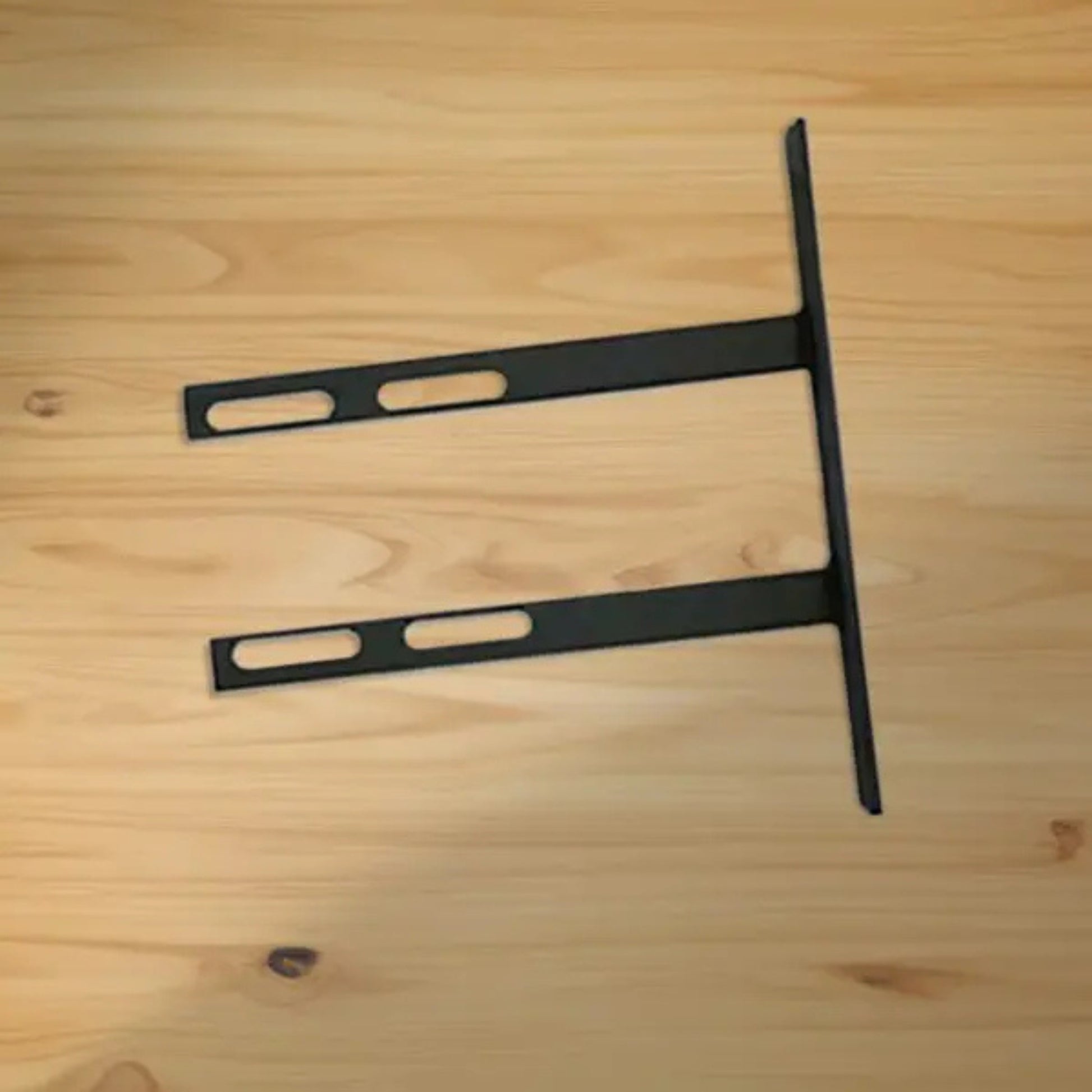 VersaClimber H/HP wall mount installation bracket in black steel finish, displayed on a wooden background for assembly or mounting guidance