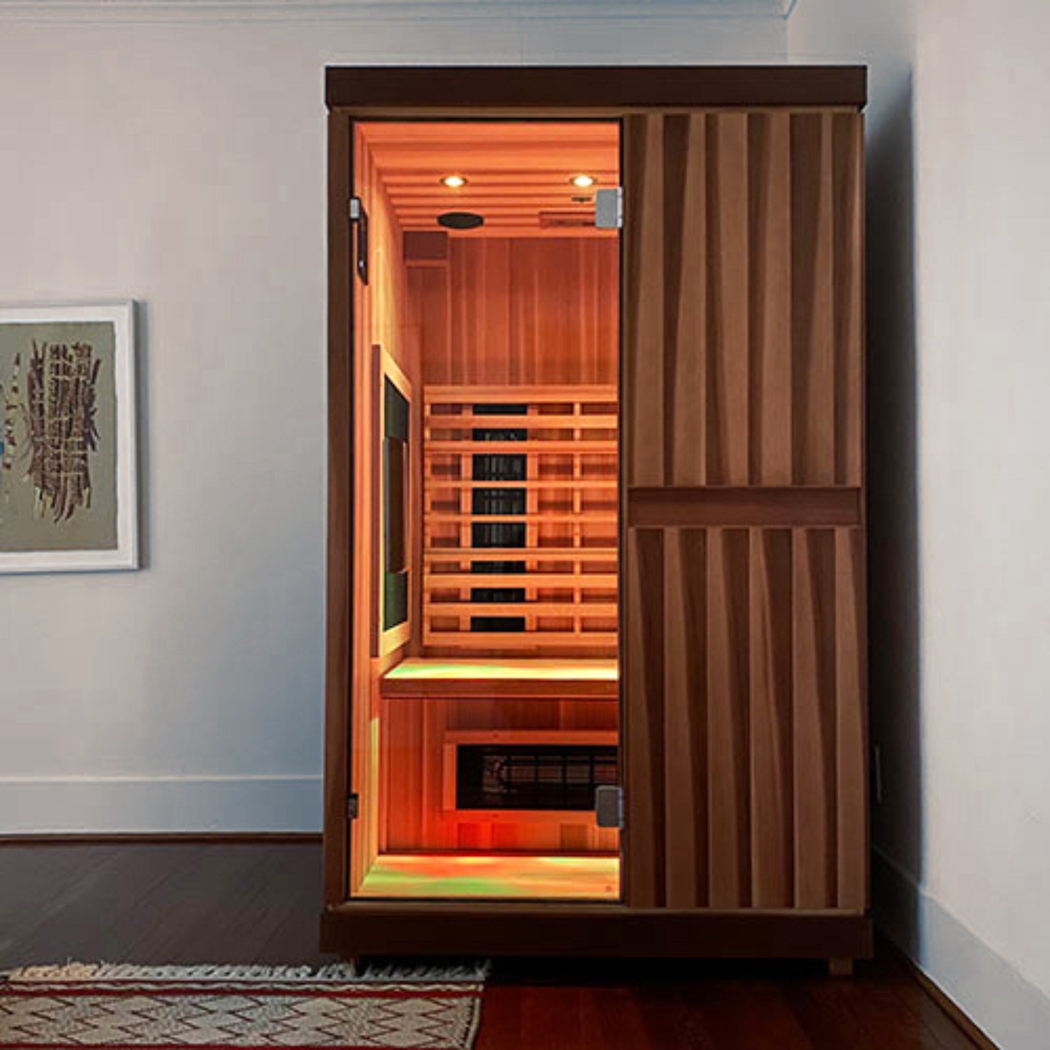 Front view of the Finnmark FD-2 infrared sauna installed in a modern indoor room with illuminated interior heater panels visible through the closed glass door.