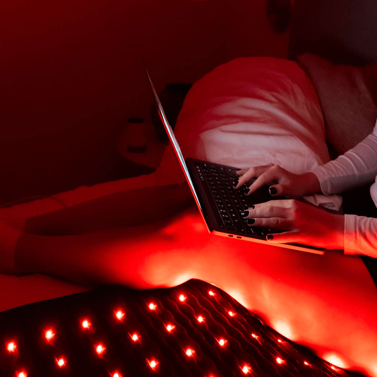 Person using a laptop while lying on a PEMF infrared heating mat with red light therapy for relaxation and focus