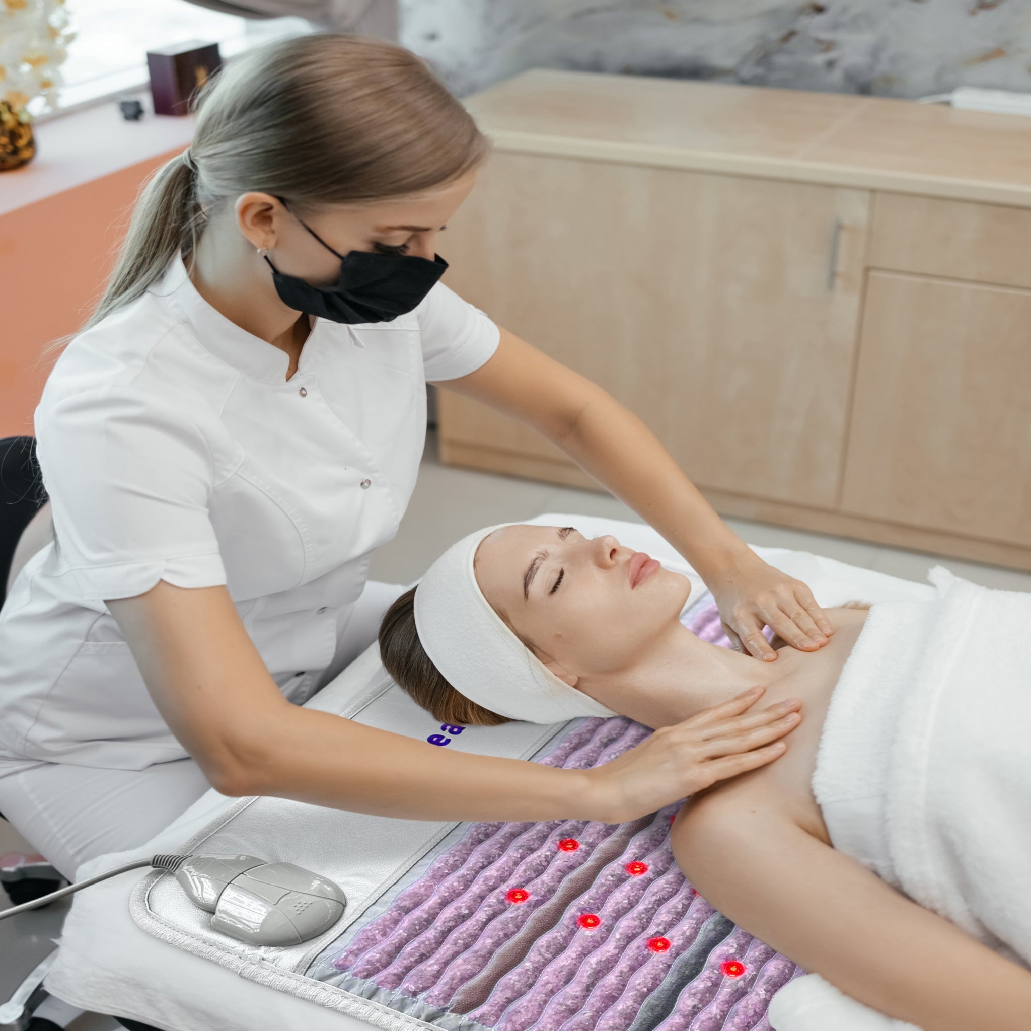 Spa professional providing facial treatment while client relaxes on HealthyLine Platinum Aura Mat Pro Plus 7428 with gemstone therapy