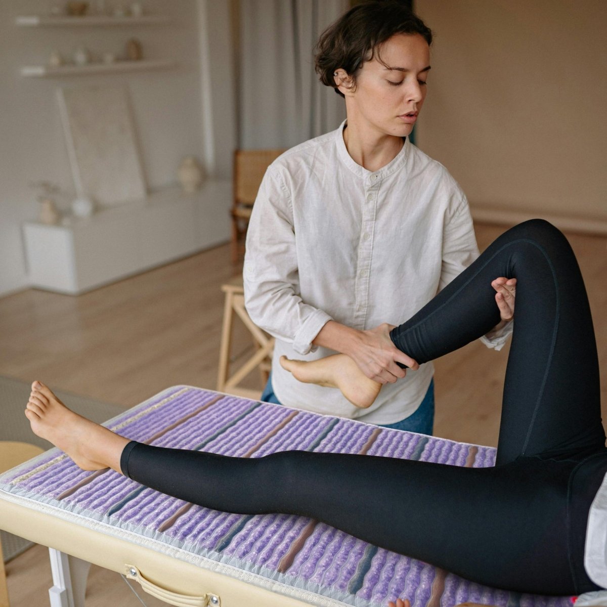 Practitioner providing foot therapy on a client using a HealthyLine Platinum PEMF Far Infrared Heating Mat with gemstones