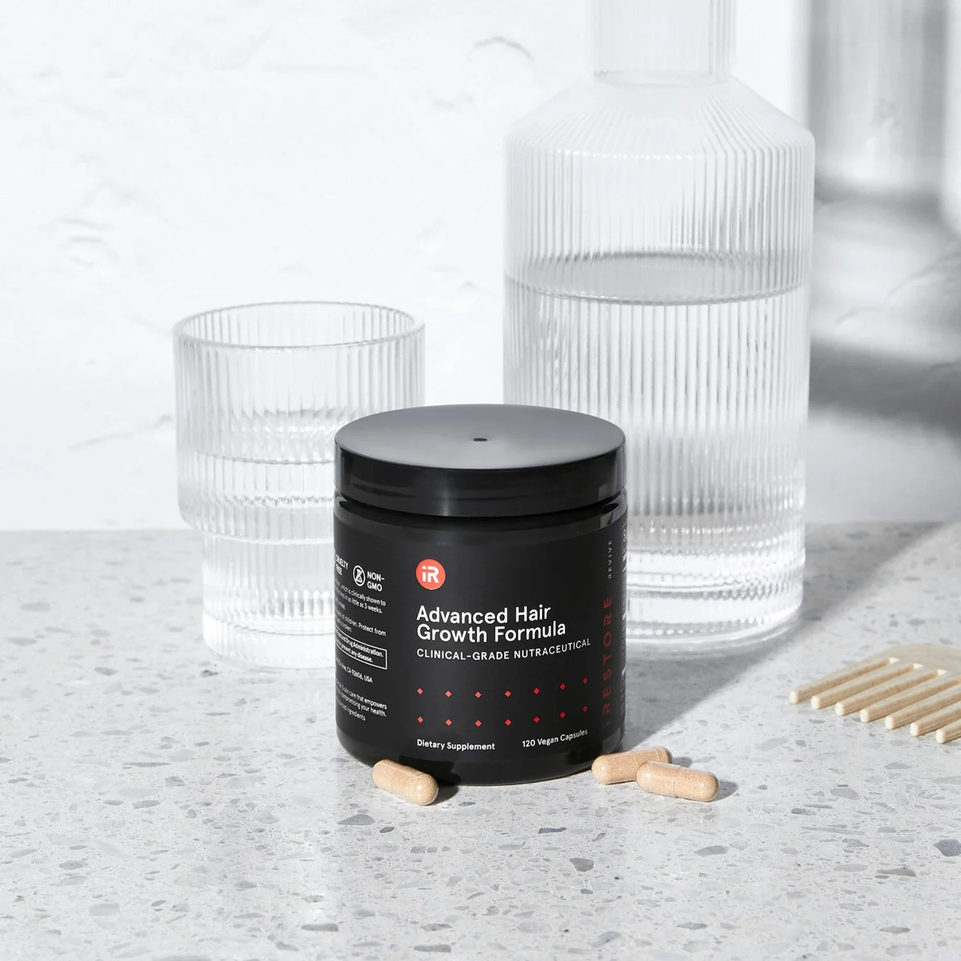 iRestore Revive hair growth supplement jar beside water glass for daily use