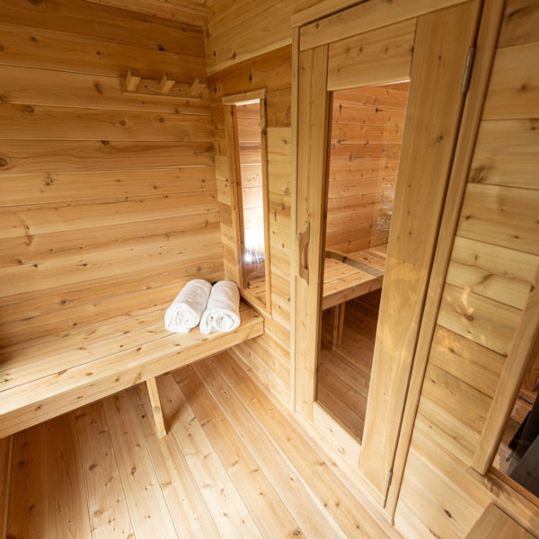 Leisurecraft CT Georgian Cabin Sauna with changeroom interior featuring cedar benches, rolled towels, and doorway to sauna room.