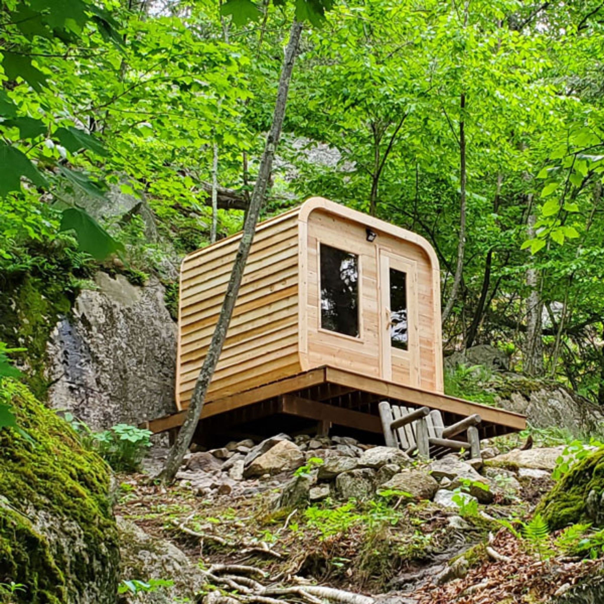 Leisurecraft CT Luna outdoor cedar sauna with modern glass front set in forest surrounded by trees and rocks.