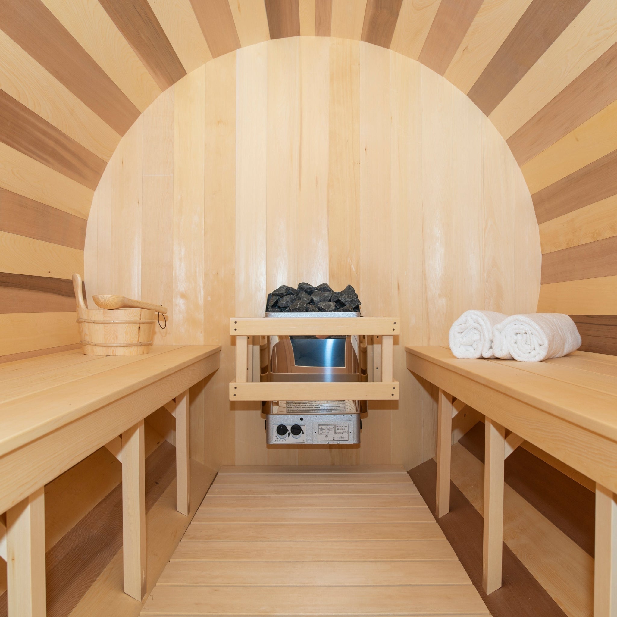 Leisurecraft CT Tranquility Barrel Sauna interior featuring smooth cedar benches, a sauna heater with stones, and neatly folded white towels, highlighting warm wood tones and serene spa ambiance.