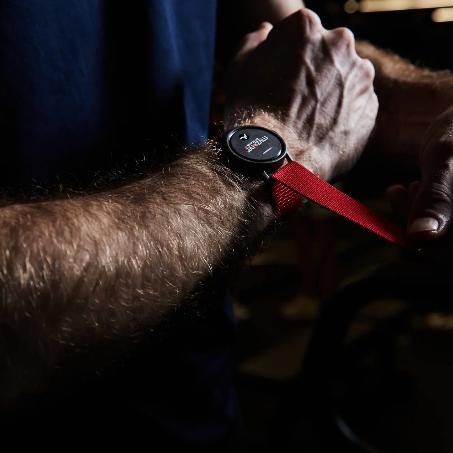 Man tightening red Myzone Switch strap on wrist, preparing for fitness session with real-time heart zone tracking technology