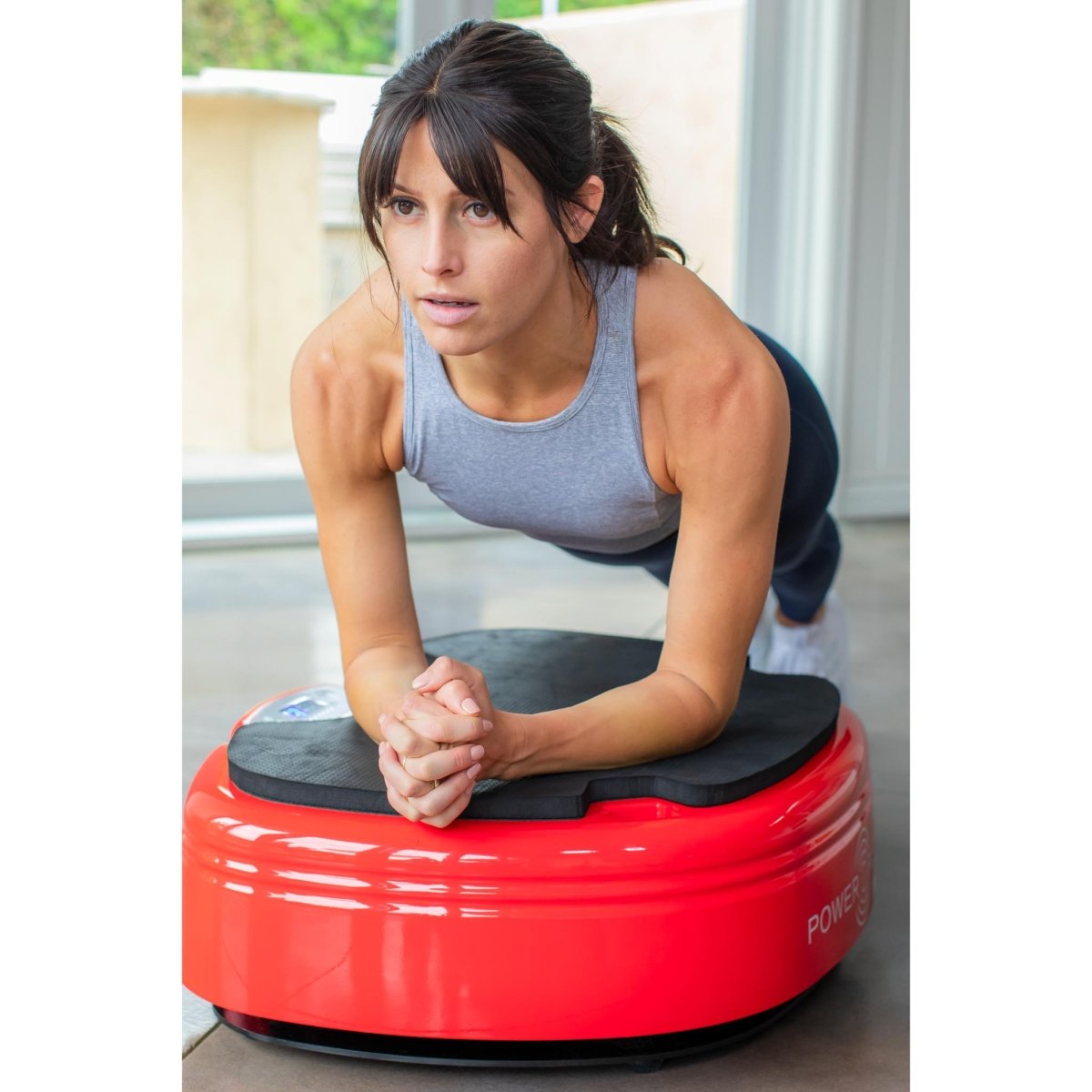 Woman performing a plank exercise on a red Power Plate MOVE vibration plate in a home setting