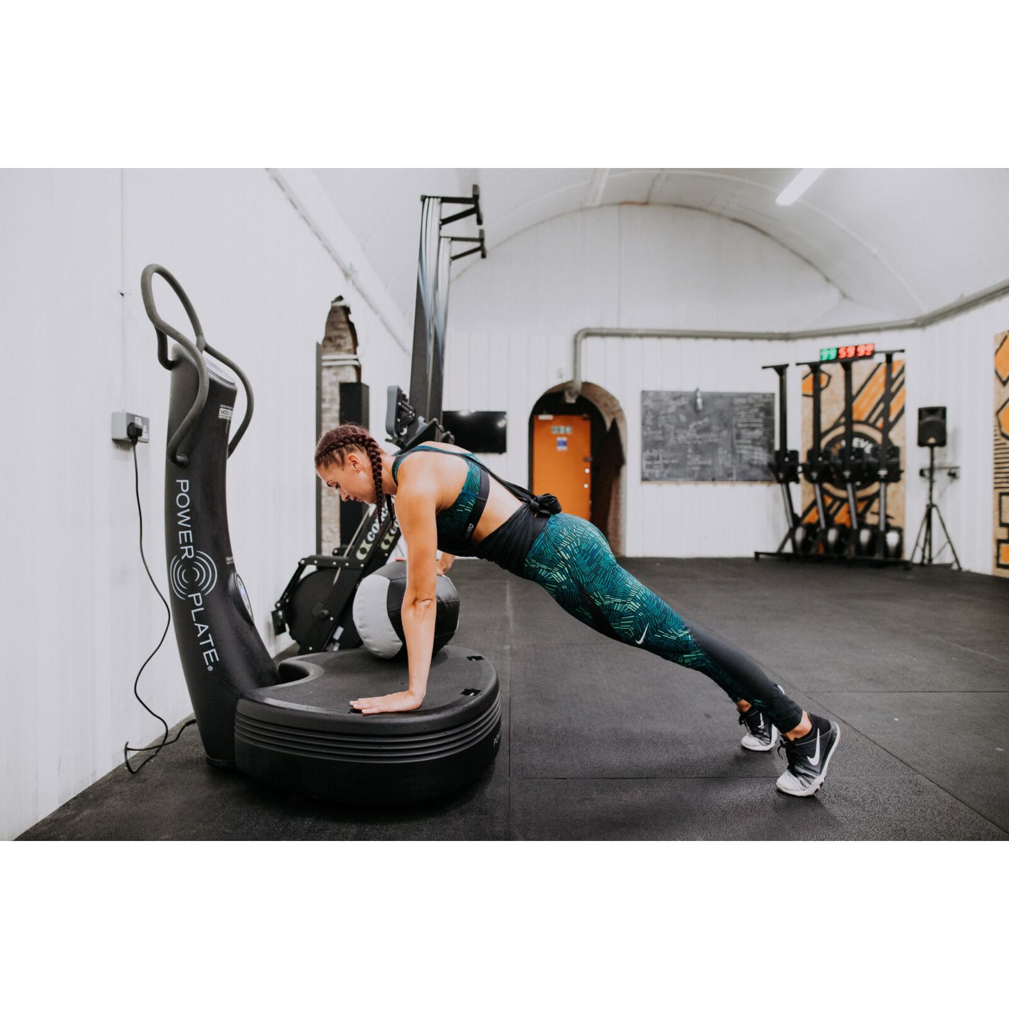 Woman performing a plank exercise on the Power Plate pro5 vibration training machine in a gym setting