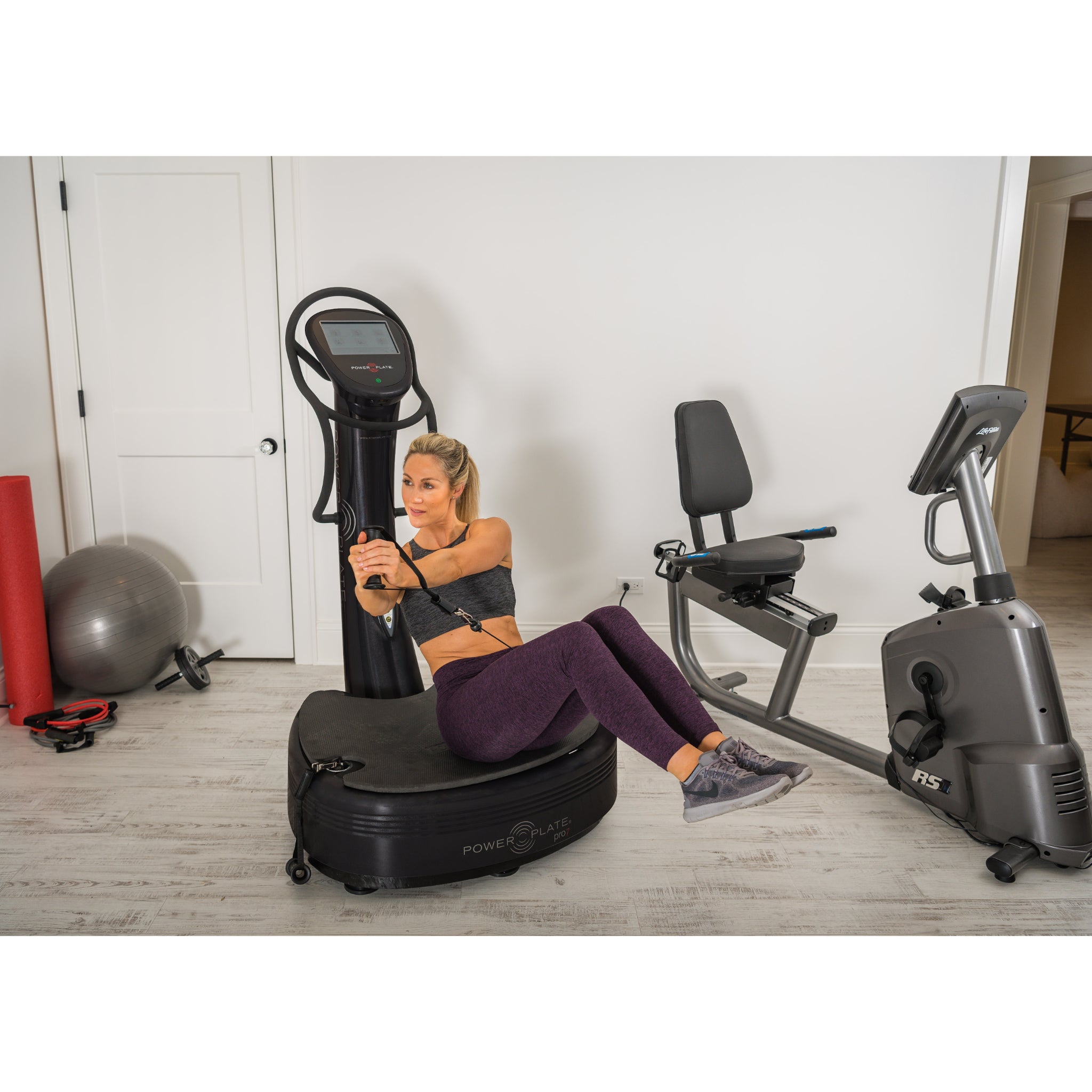 Woman performing an ab exercise on the Power Plate pro7 vibration training machine in a home gym setting