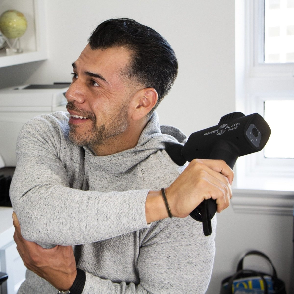 Man applying Power Plate Pulse black massage gun to shoulder for targeted muscle relief