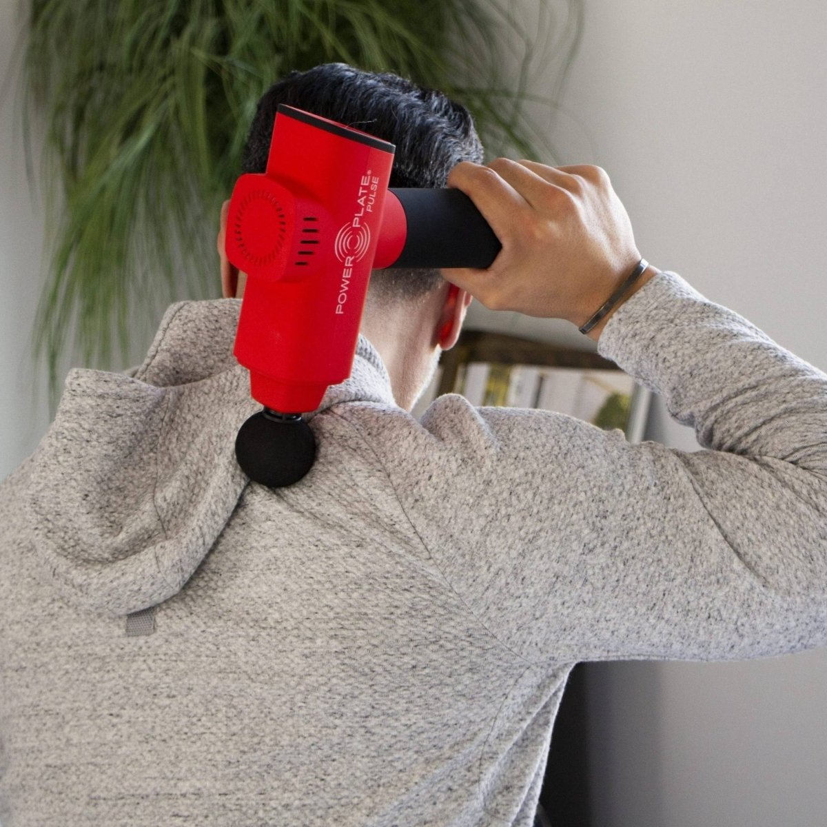 Power Plate Pulse red massage gun being used on upper back and shoulders for deep muscle relief

