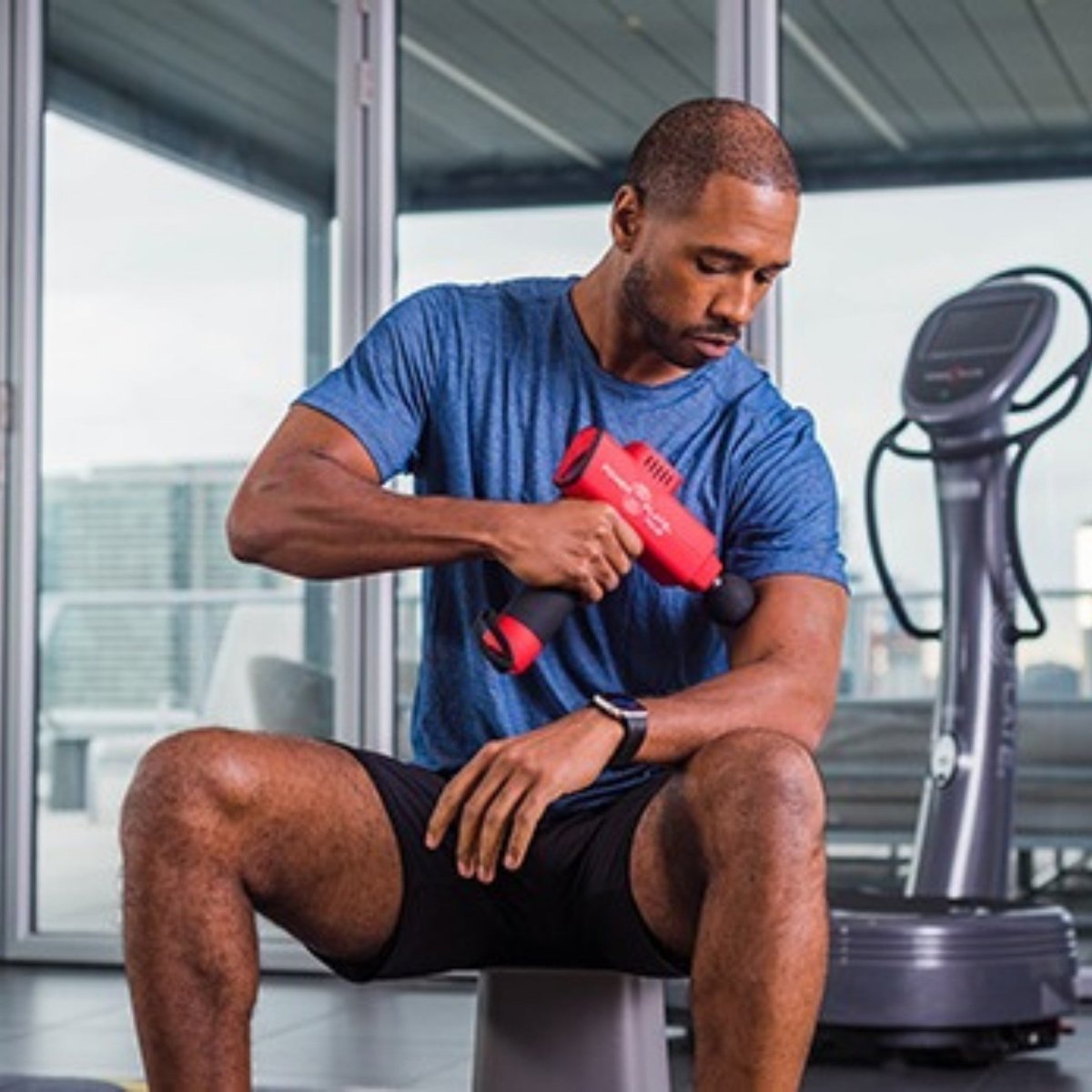 Athlete using Power Plate Pulse massage gun on arm for muscle recovery in gym setting