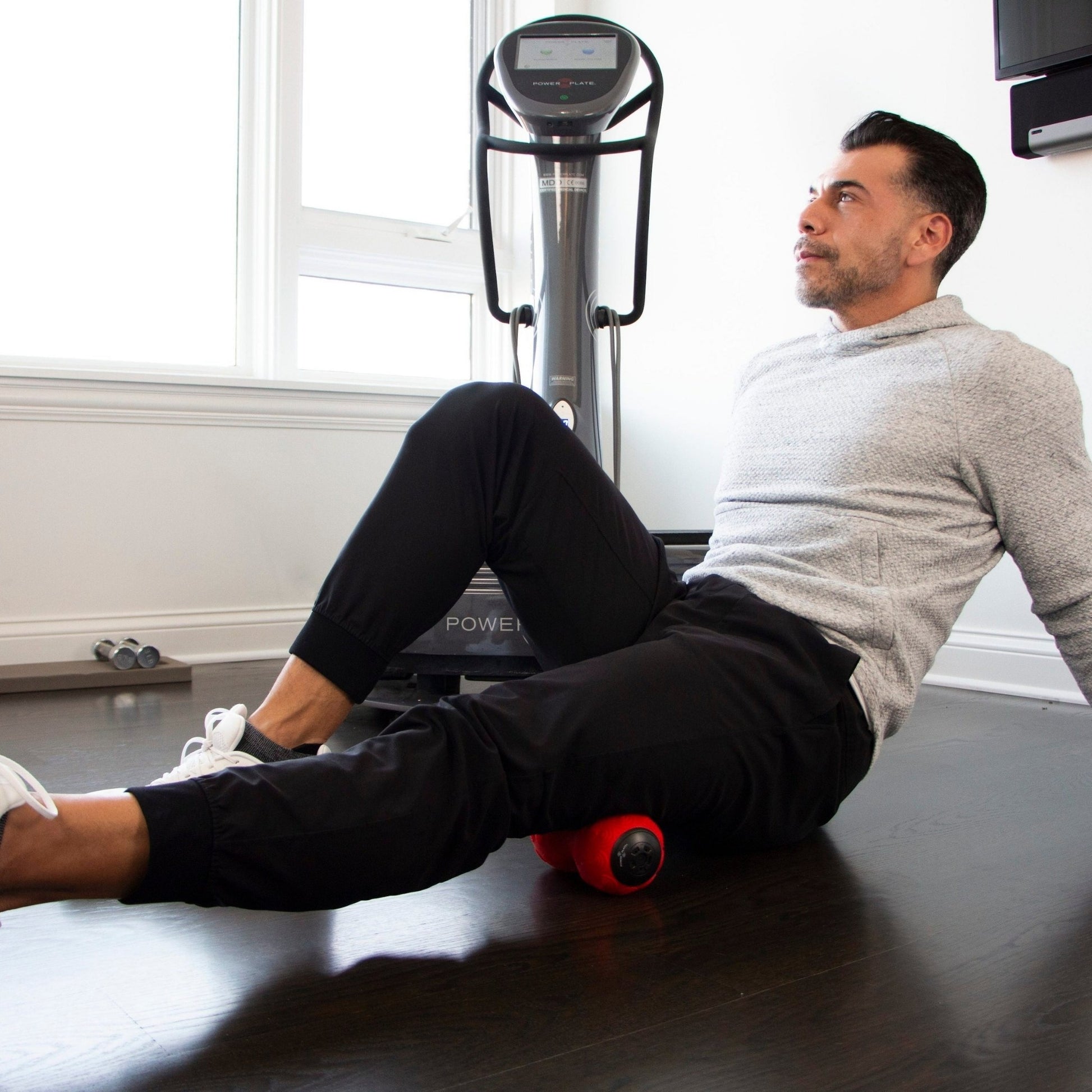 Man using Power Plate vibrating roller on upper hamstrings for muscle recovery at home